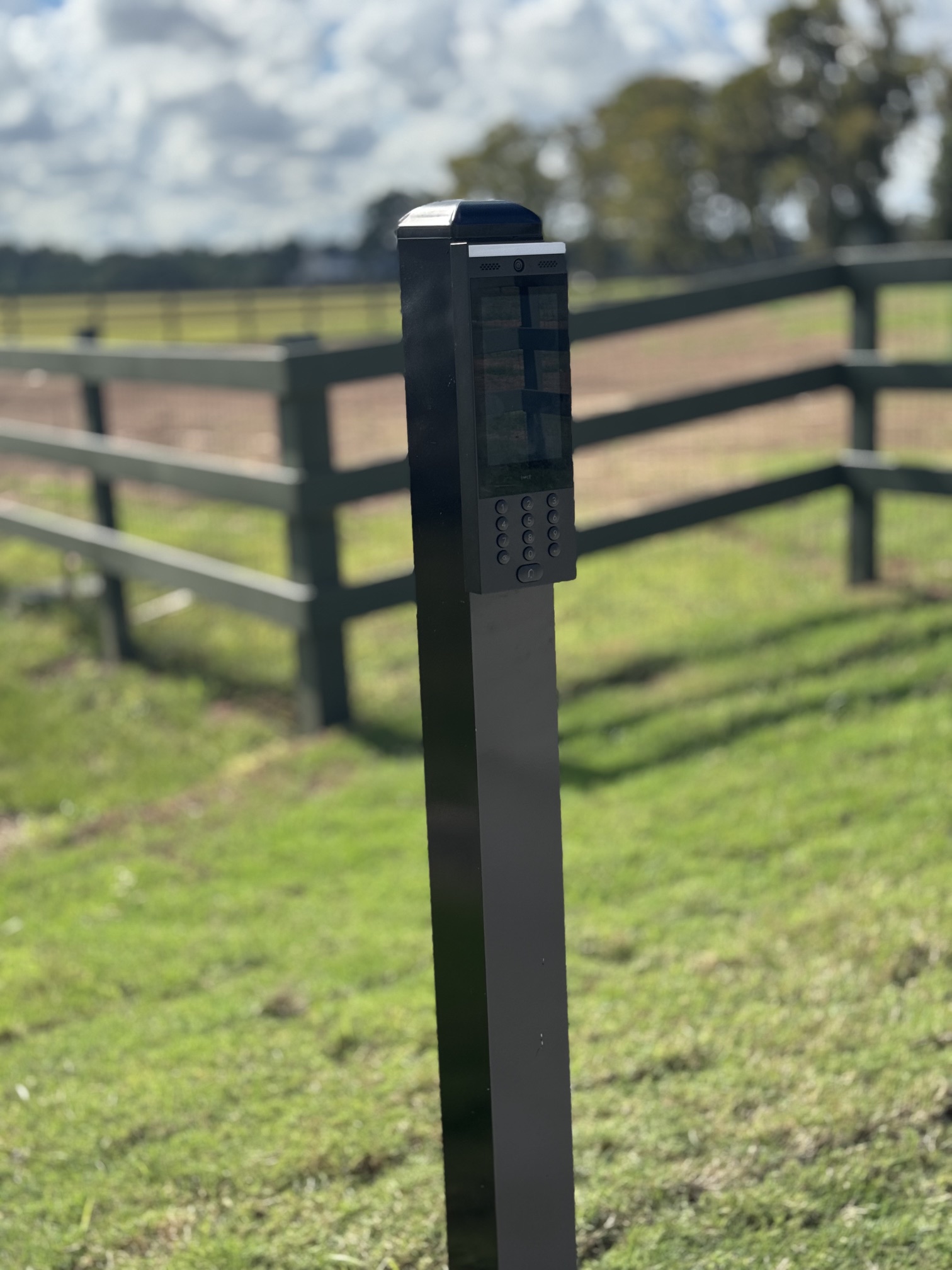 Gate video intercom keypad on black post with horse pasture in background